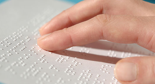 Слика од човечка рака како допира лист со брајов текст.